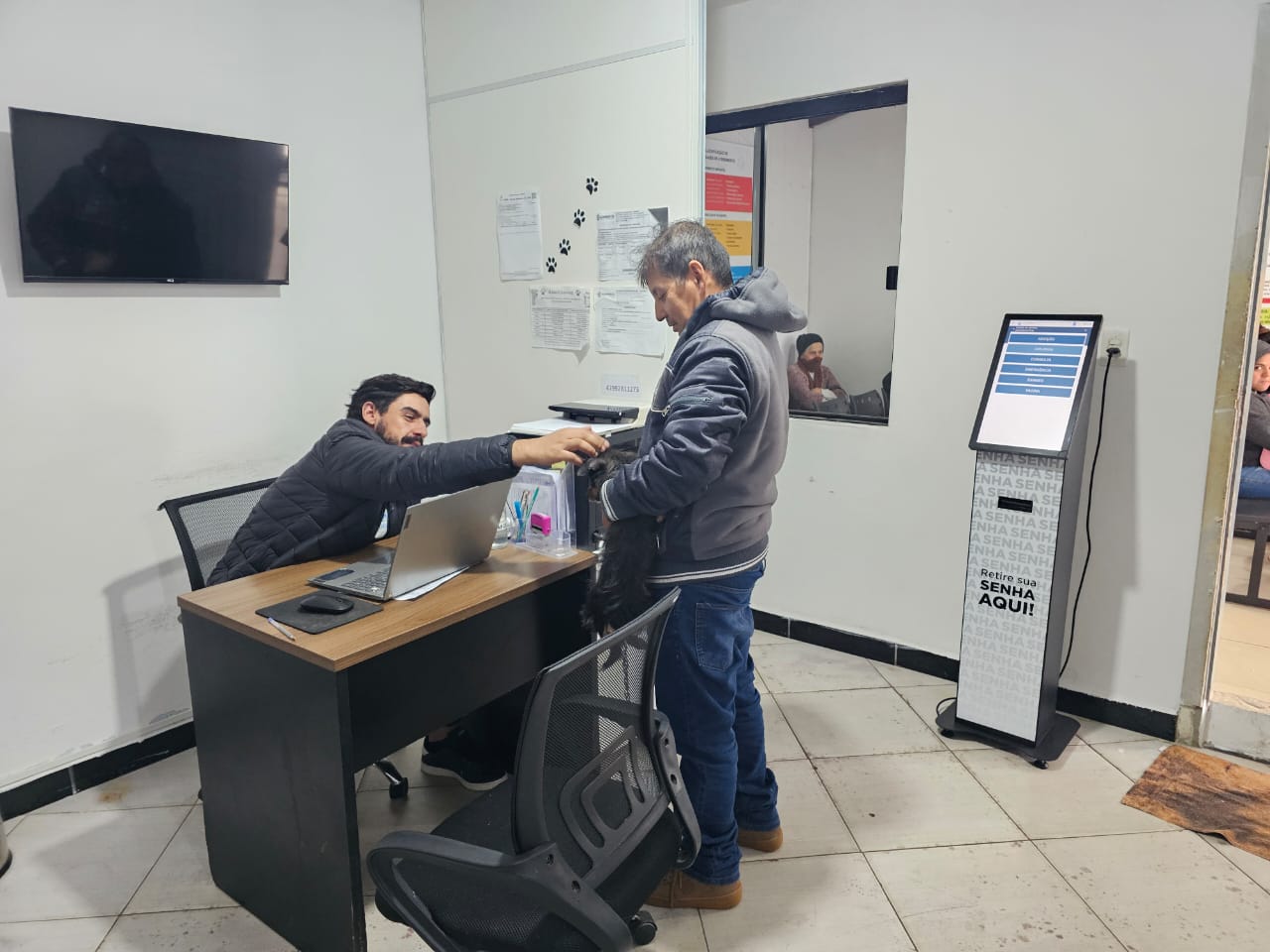 Recepção do hospital veterinário com totem de senha e tutor sendo atendido com seu pet